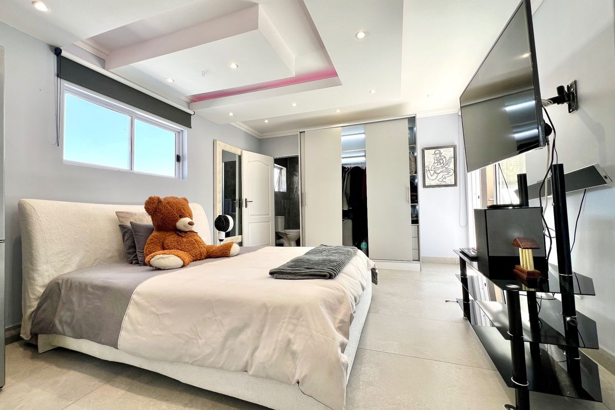 Spacious bedroom featuring a modern recessed ceiling with integrated lighting, large format floor tiles, and a built-in sliding door wardrobe.
