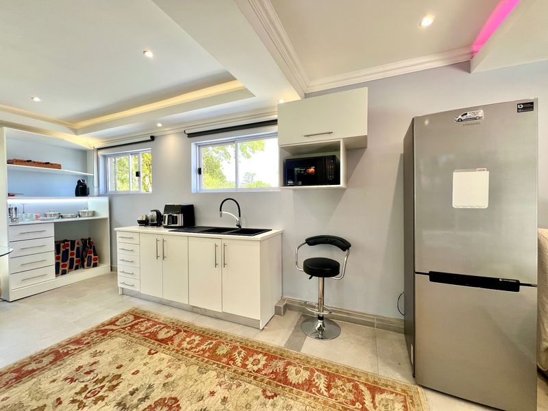 A modern, well-lit kitchen area featuring white cabinetry, a sleek black sink with a gooseneck faucet, and recessed ceiling lighting.