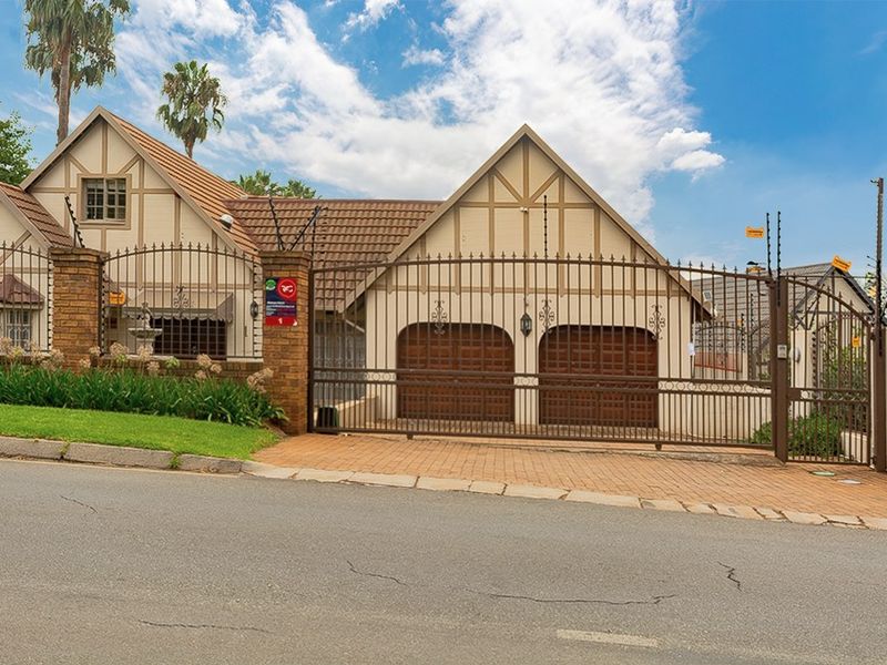 Front elevation of a house featuring a double garage, secure gated entrance, and electric fencing, showcasing a well-maintained exterior facade.