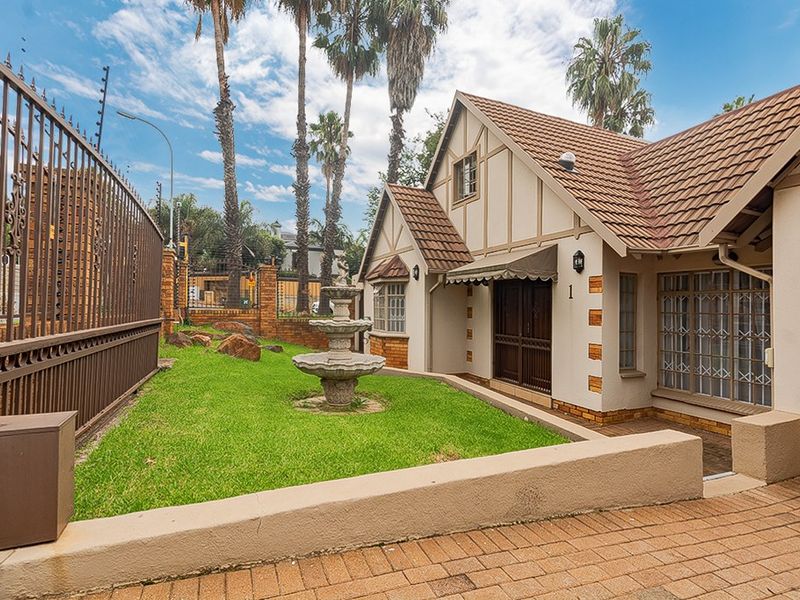 Front facade of a charming home featuring a tiled roof, brick-paved driveway, secure metal fencing, and a decorative stone fountain in the front garden.