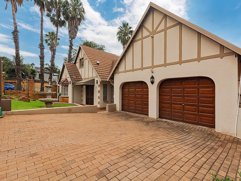 Front elevation of a charming Tudor-style home featuring a double garage, brick-paved driveway, and a landscaped garden with a decorative stone fountain.