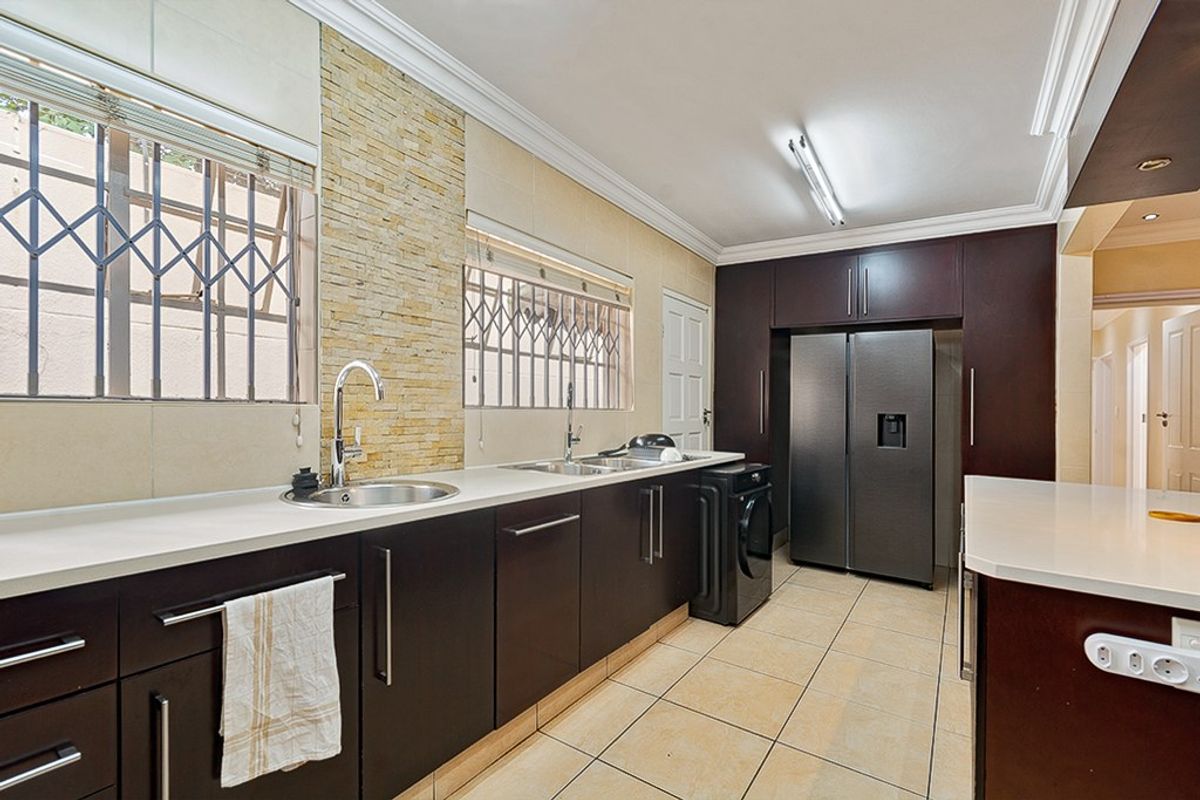 Modern kitchen featuring dark wood cabinetry, stone countertops, double sink, and decorative stone wall accents with tiled flooring and secure window fittings.