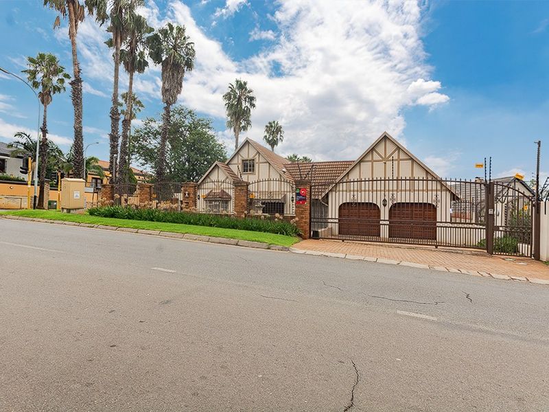 Street view of the property featuring a double garage, secure wrought iron gate, and established perimeter wall with electric fencing.