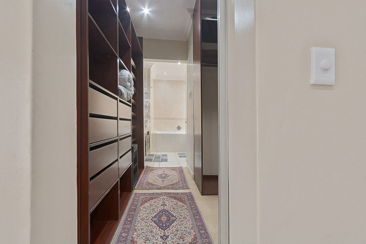 A well-organized walk-in closet featuring extensive built-in cabinetry and shelving, providing ample storage space with direct access to the adjoining bathroom.