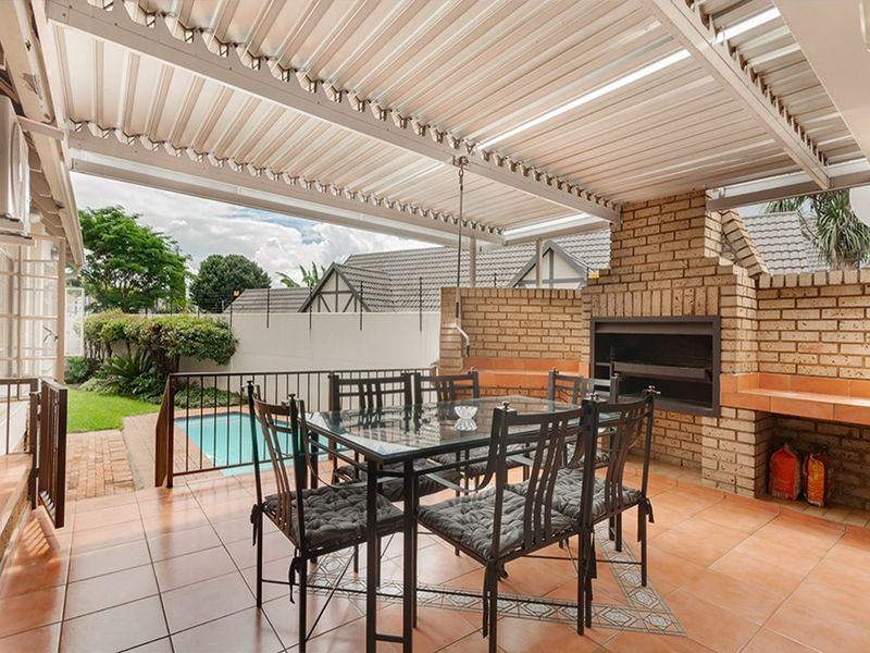 Covered outdoor patio featuring a built-in brick braai, tiled flooring, and direct access to the garden and swimming pool area.