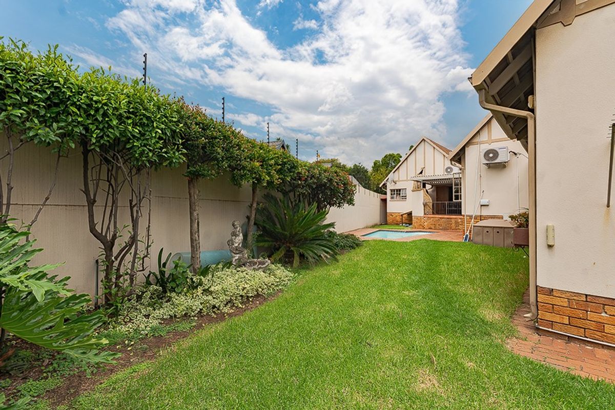 A well-maintained rear garden featuring a swimming pool, brick-paved patio area, and secure boundary walls with electric fencing.
