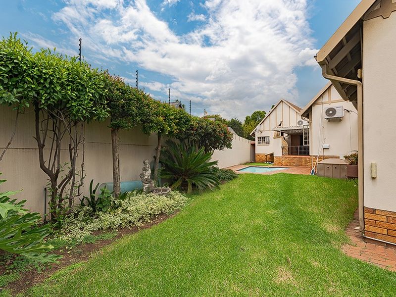 A well-maintained rear garden featuring a swimming pool, brick-paved patio area, and secure boundary walls with electric fencing.