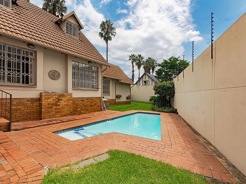 Rear exterior view featuring a swimming pool, brick paved surround, and perimeter wall with electric fencing.
