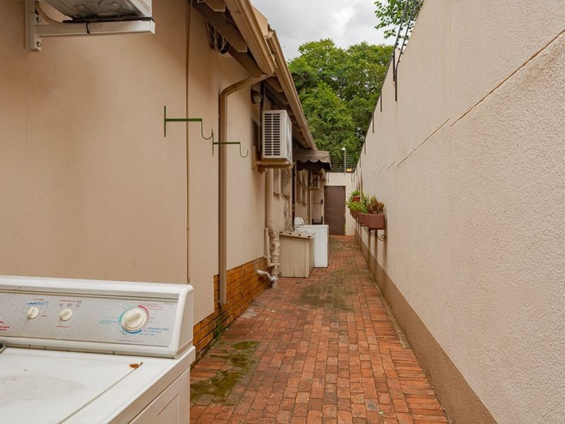 A narrow side utility passage featuring brick paving, exterior wall access, and mounted air conditioning units.