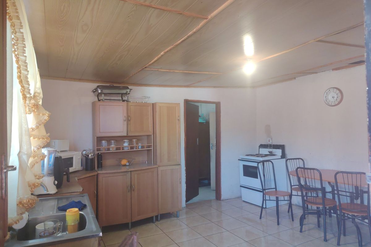 A functional kitchen featuring wooden cabinetry, tiled flooring, and a wooden ceiling, providing a basic layout with a freestanding stove.