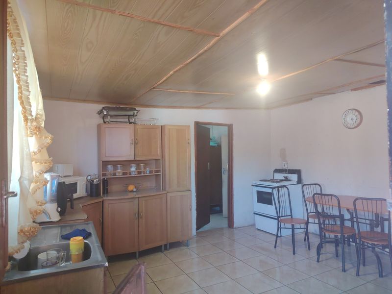 A functional kitchen featuring wooden cabinetry, tiled flooring, and a wooden ceiling, providing a basic layout with a freestanding stove.