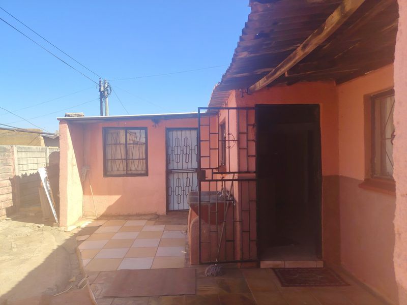 Rear exterior view of the property featuring a small tiled patio area, security gates, and a built-in concrete wash basin.