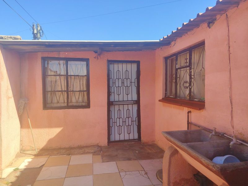 Rear exterior view featuring a concrete laundry sink, security gate, and tiled patio area with visible wear to the wall plaster and finishes.
