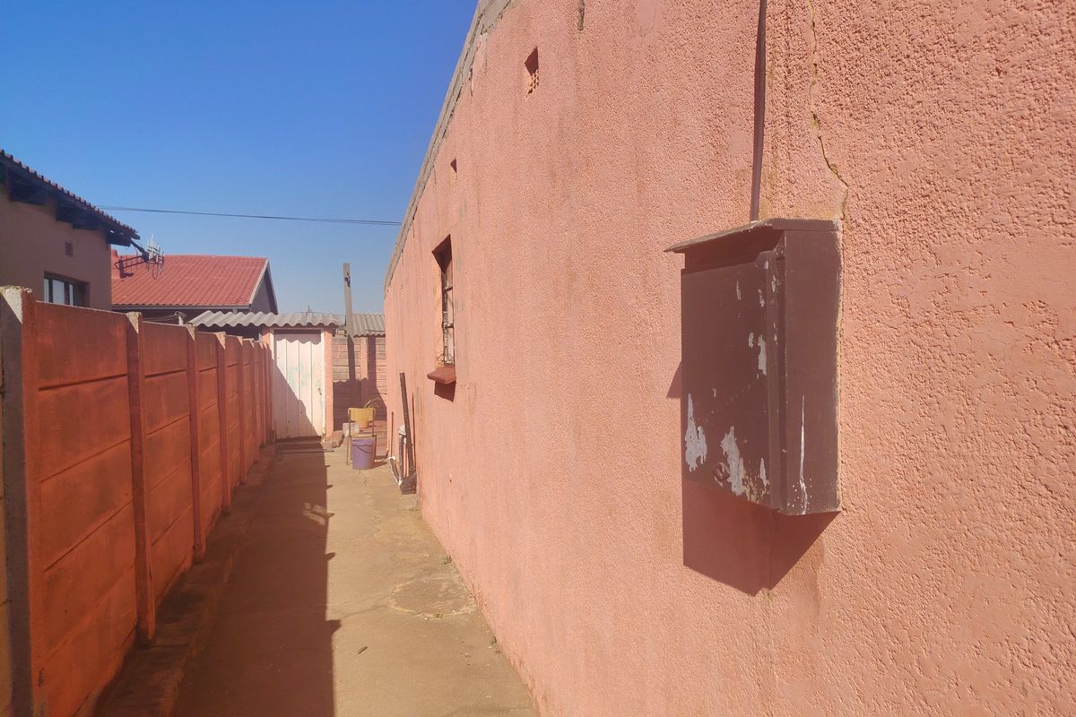 Side exterior passage featuring a concrete pathway, precast boundary wall, and an external electrical distribution box mounted on the plastered wall.