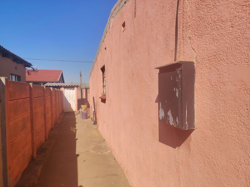 Side exterior passage featuring a concrete pathway, precast boundary wall, and an external electrical distribution box mounted on the plastered wall.