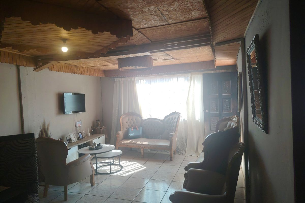A living room featuring tiled flooring and a distinctive wooden panelled ceiling with decorative trim, offering a dated aesthetic ready for modernization.