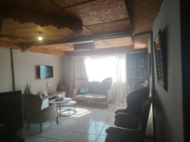 A living room featuring tiled flooring and a distinctive wooden panelled ceiling with decorative trim, offering a dated aesthetic ready for modernization.