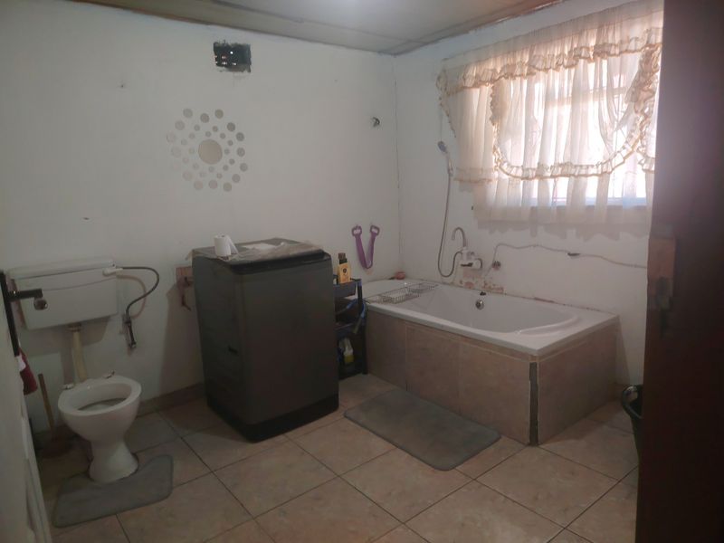 A dated bathroom featuring a standard toilet, bathtub with tiled surround, and tiled flooring, currently showing signs of wear and unfinished wall surfaces.
