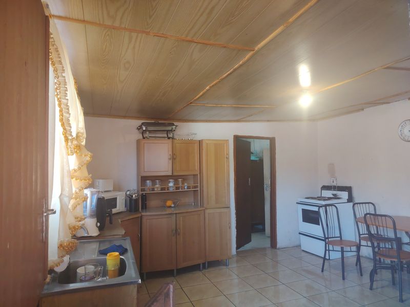 A functional kitchen featuring wooden cabinetry, tiled flooring, and a timber panelled ceiling, offering a dated aesthetic with potential for modernization.