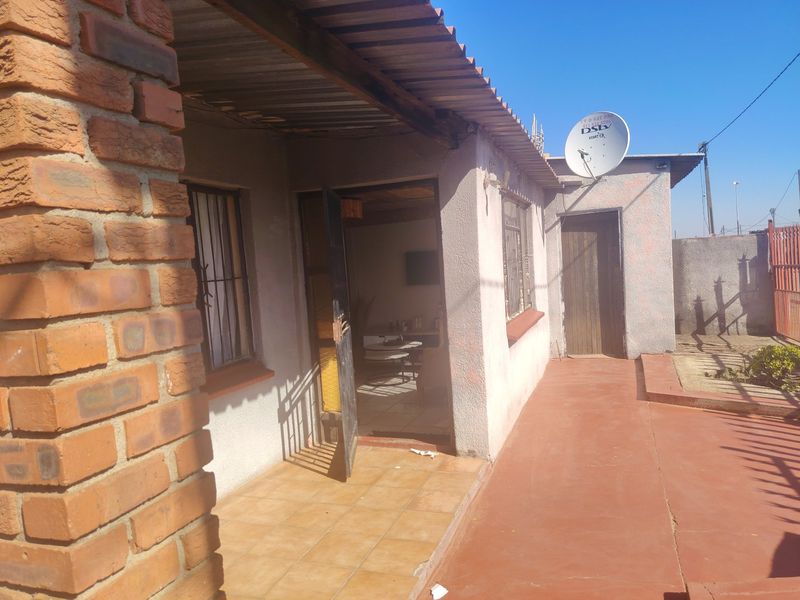 Rear exterior view of the property featuring a covered patio area, brick pillar detailing, and a paved walkway.