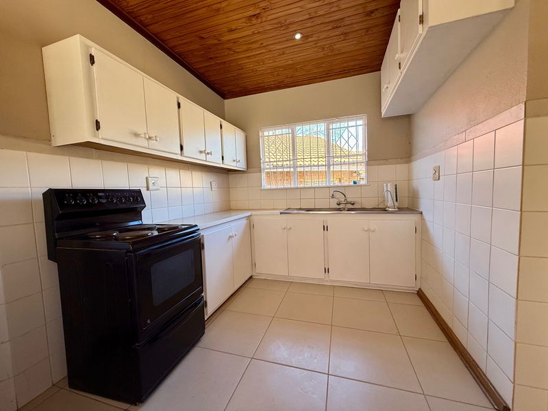 A functional kitchen featuring white cabinetry, tiled backsplash, tiled flooring, and a timber ceiling, offering a clean space ready for modern updates.