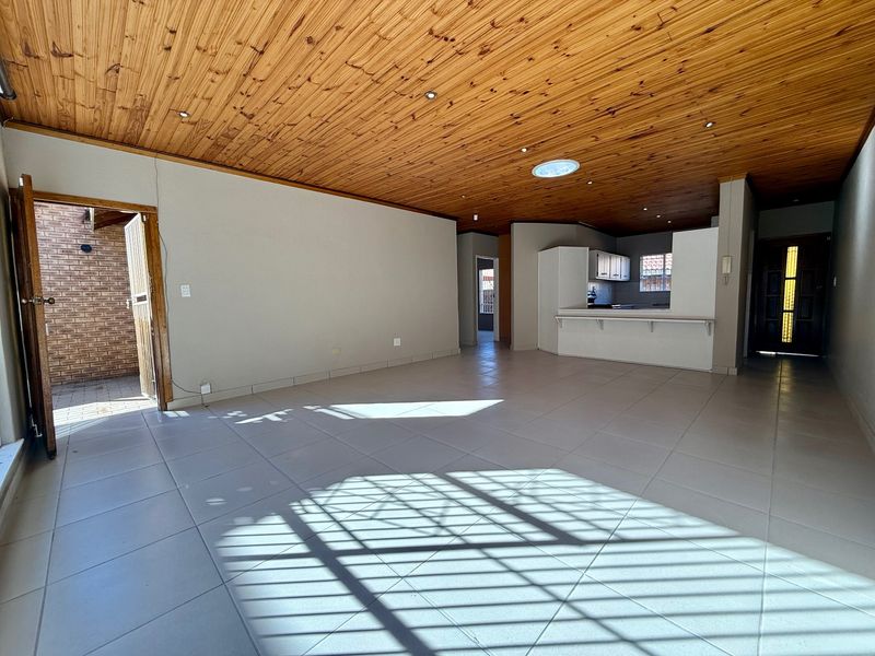 Spacious open-plan living area featuring a timber ceiling, ceramic floor tiles, and a breakfast counter connecting to the kitchen.
