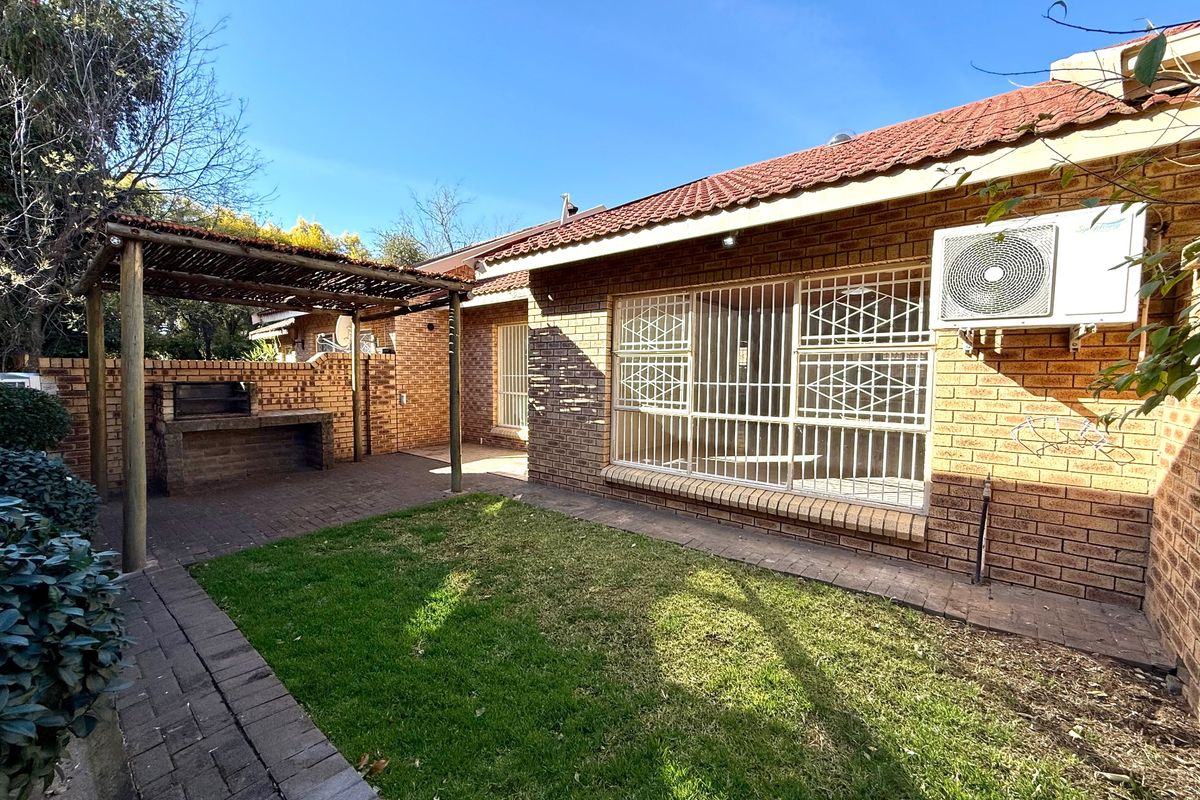 Rear exterior view of the townhouse featuring a paved patio area with a built-in braai, pergola, and a small private garden.