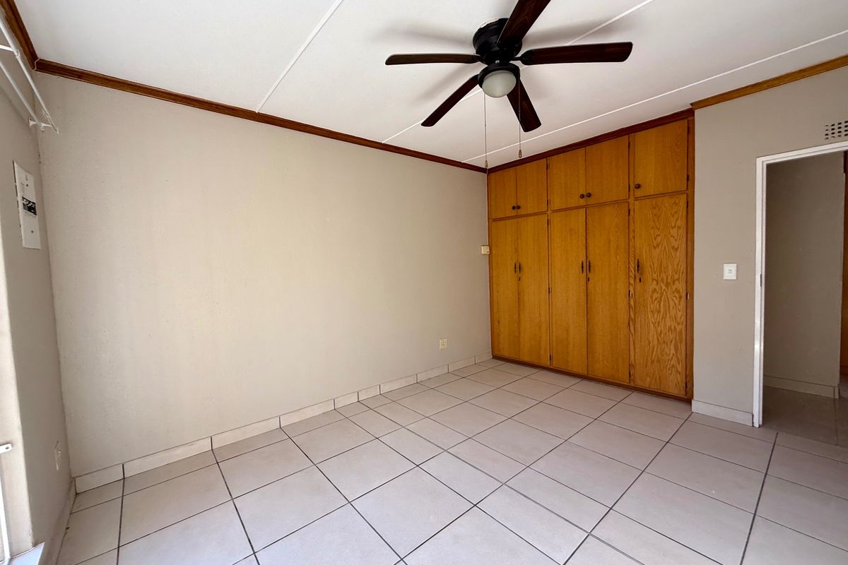 A spacious, empty bedroom featuring neutral tiled flooring, a ceiling fan, and ample built-in wooden cabinetry for storage.