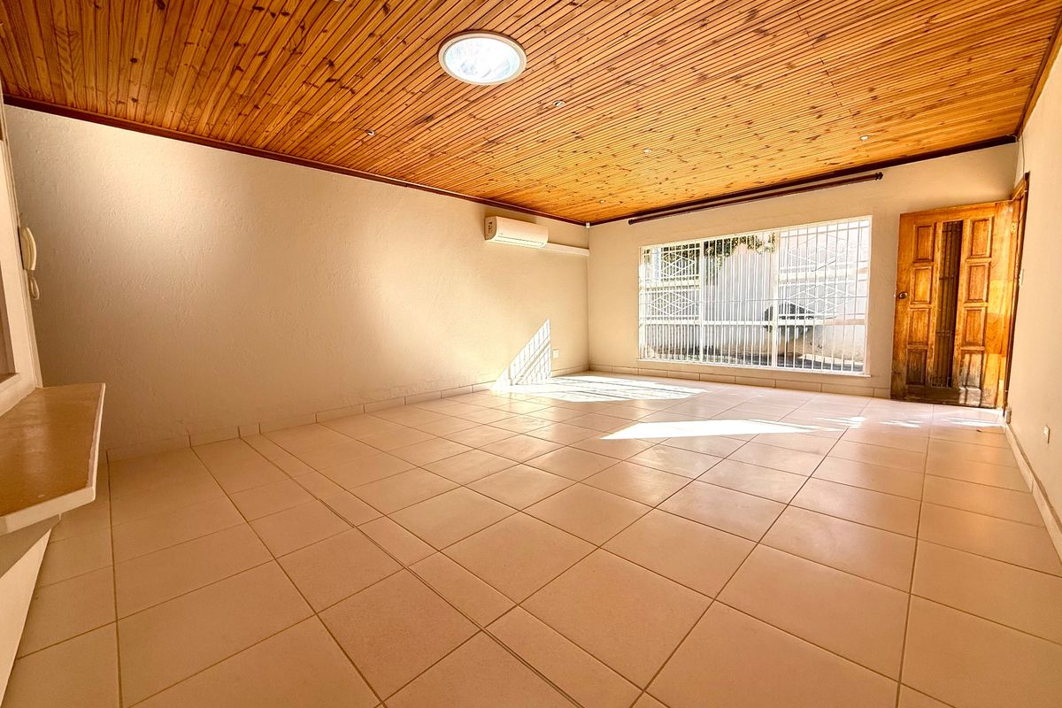 Spacious living area featuring ceramic floor tiles, a timber-clad ceiling with a skylight, and a wall-mounted air conditioning unit.