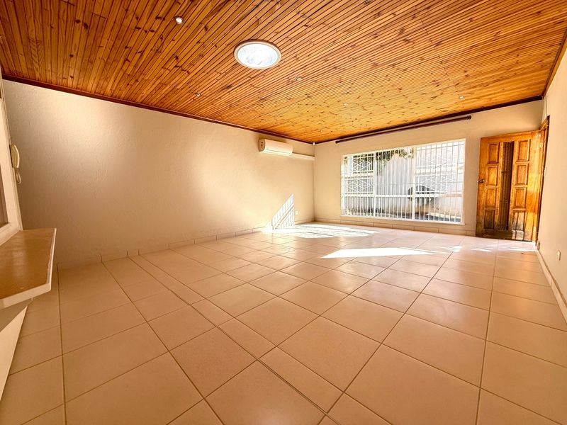 Spacious living area featuring ceramic floor tiles, a timber-clad ceiling with a skylight, and a wall-mounted air conditioning unit.