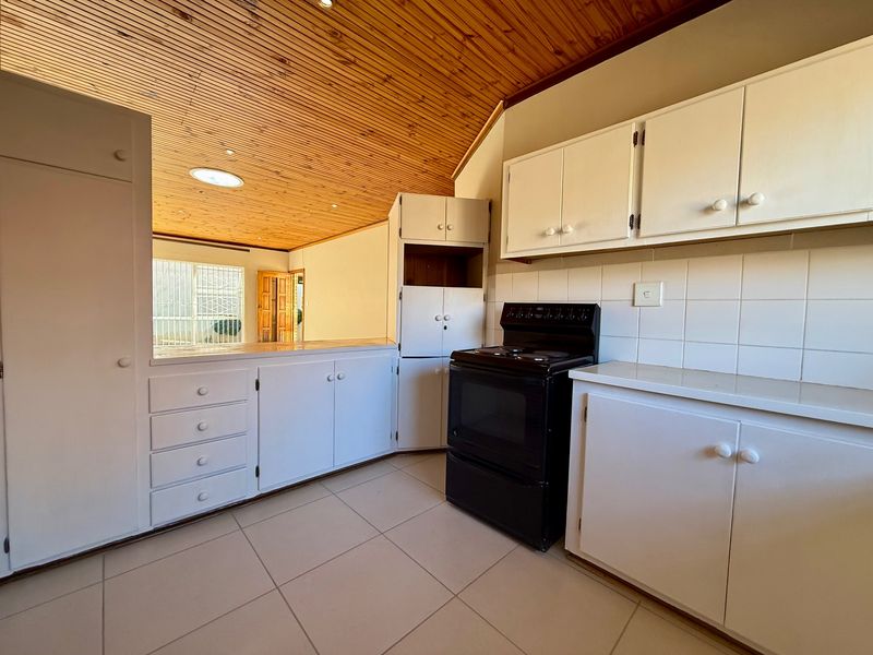 A functional kitchen featuring white cabinetry, tiled backsplash, a freestanding stove, and a distinctive timber tongue and groove ceiling with a skylight.