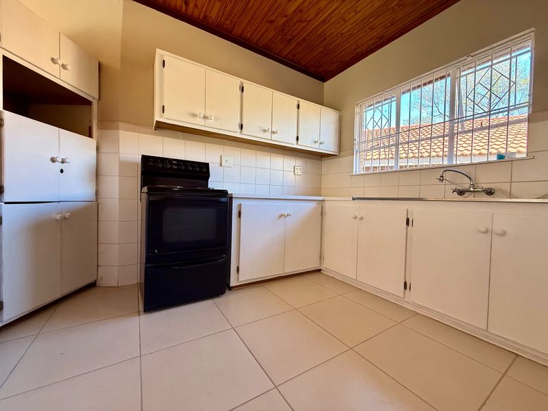 A functional kitchen featuring white built-in cabinetry, tiled splashbacks, a stainless steel sink, and a timber ceiling, offering a clean and practical layout.
