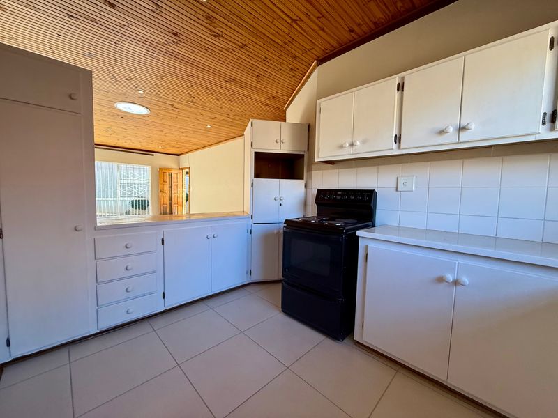 A functional kitchen featuring white cabinetry, a tiled backsplash, a freestanding oven, and a distinctive timber-clad ceiling with a skylight.