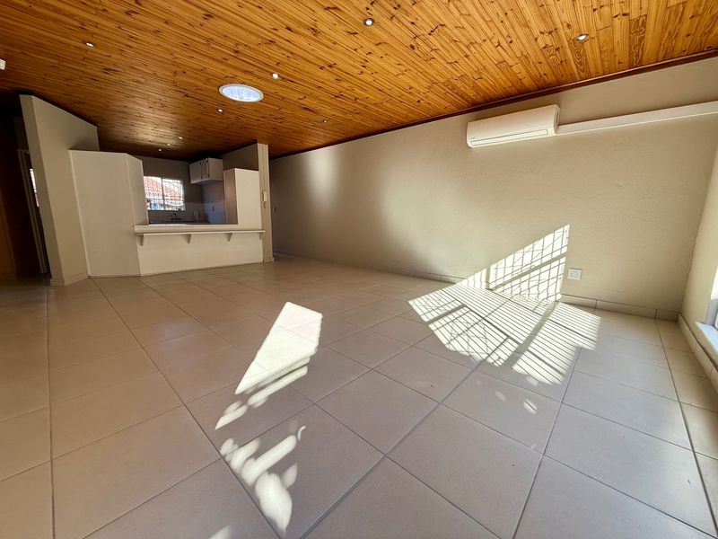 Spacious open-plan living area featuring a timber ceiling, tiled flooring, split-system air conditioning, and an integrated kitchen breakfast bar.