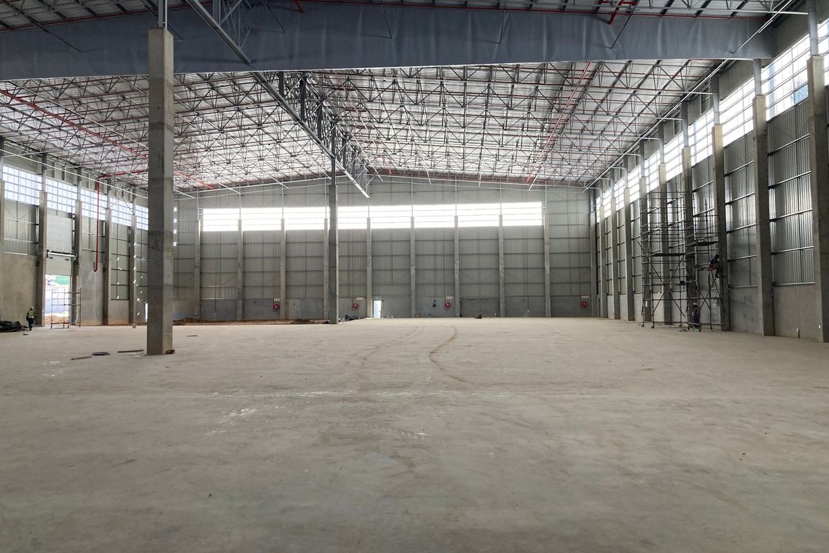 Spacious industrial warehouse interior featuring high ceilings, exposed steel truss roofing, concrete flooring, and fire sprinkler systems, currently in a clean, unfinished state.