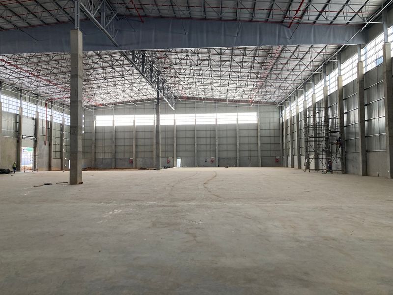 Spacious industrial warehouse interior featuring high ceilings, exposed steel truss roofing, concrete flooring, and fire sprinkler systems, currently in a clean, unfinished state.
