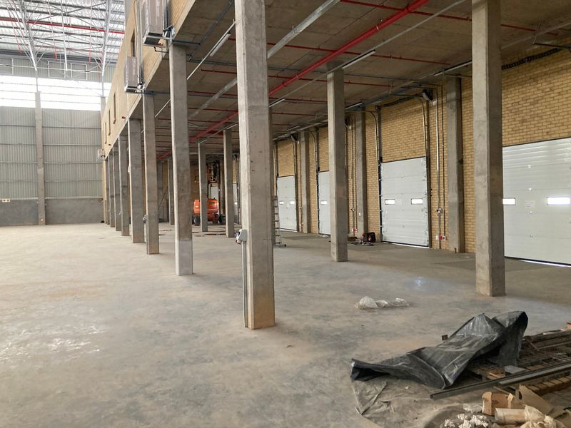 Spacious industrial warehouse interior featuring high ceilings, concrete flooring, exposed structural columns, and multiple roller shutter loading doors.