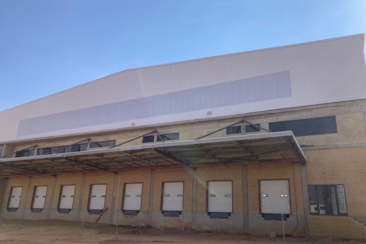 Industrial warehouse exterior featuring multiple loading docks with roller shutter doors, a steel canopy, and metal cladding under construction.