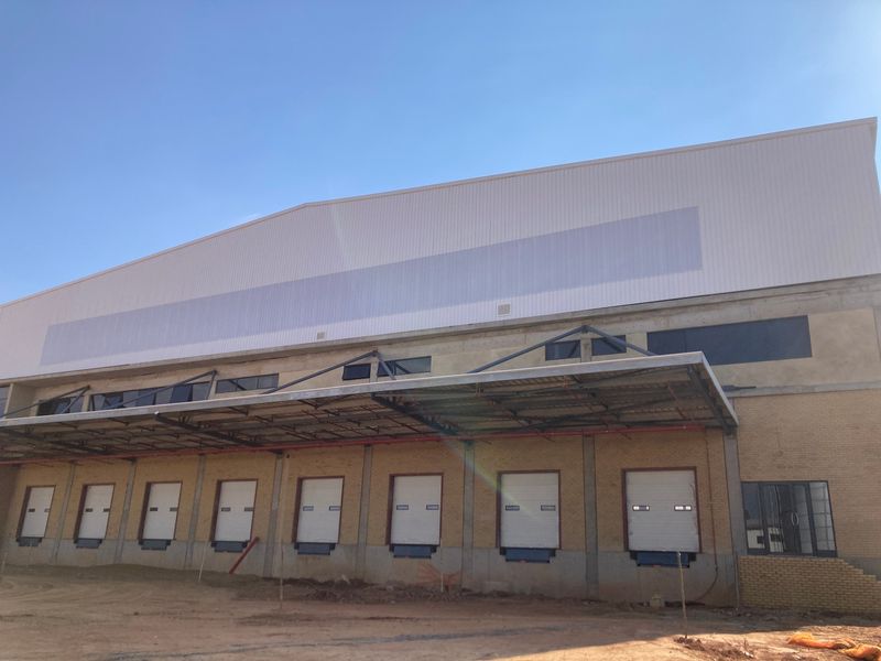 Industrial warehouse exterior featuring multiple loading docks with roller shutter doors, a steel canopy, and metal cladding under construction.