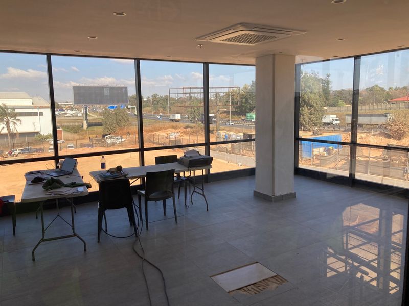 Open-plan office space featuring floor-to-ceiling windows with highway views, recessed lighting, and ceiling-mounted air conditioning.
