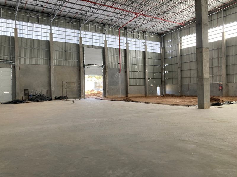 Spacious industrial warehouse unit featuring high ceilings, exposed steel trusses, concrete flooring, and large roller shutter doors for easy access.