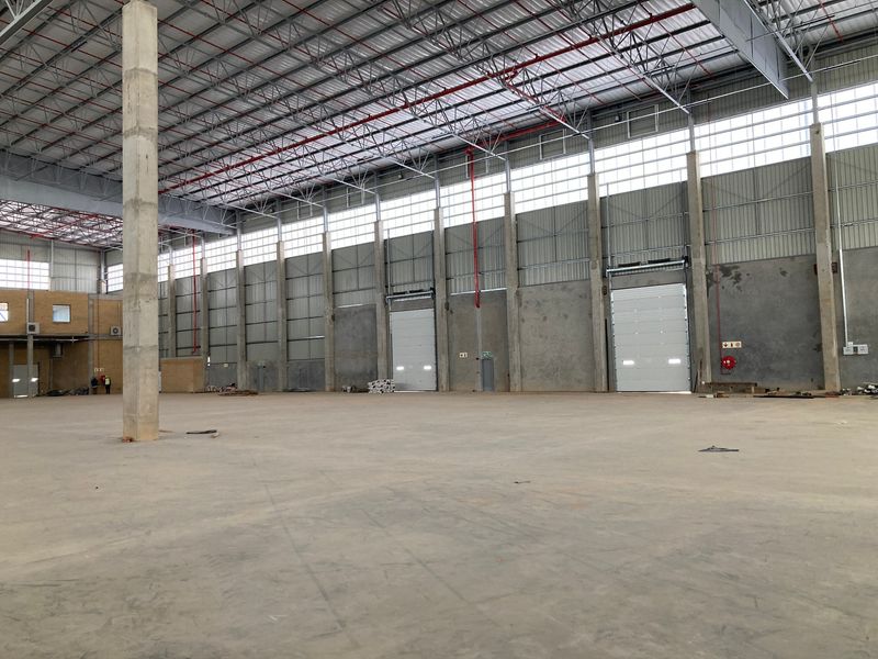 Spacious industrial warehouse featuring high ceilings, exposed steel trusses, fire sprinkler system, and multiple roller shutter doors for efficient logistics and storage operations.
