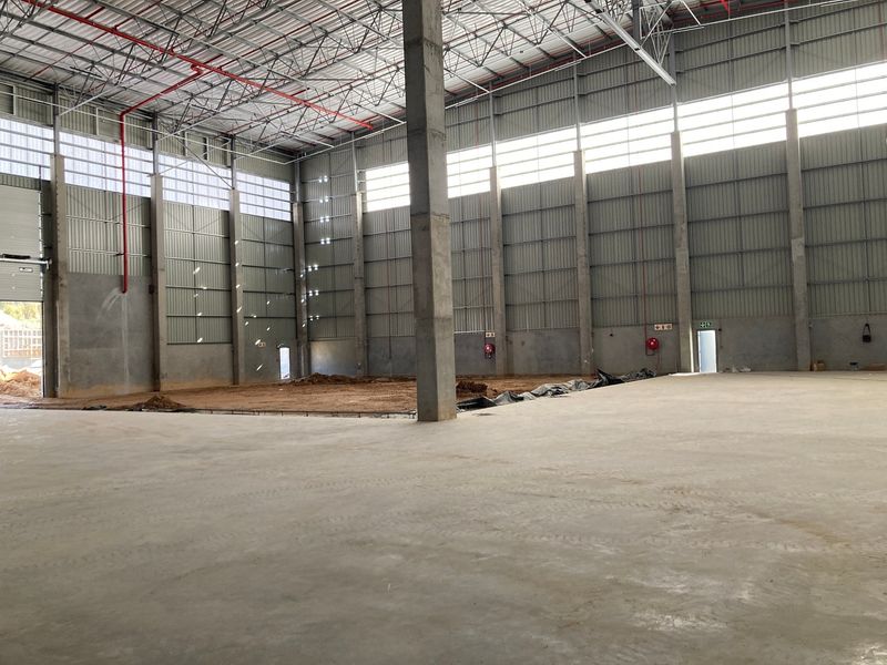 Spacious industrial warehouse interior featuring high ceilings, exposed steel trusses, concrete flooring, and fire sprinkler systems, currently in an unfinished state.