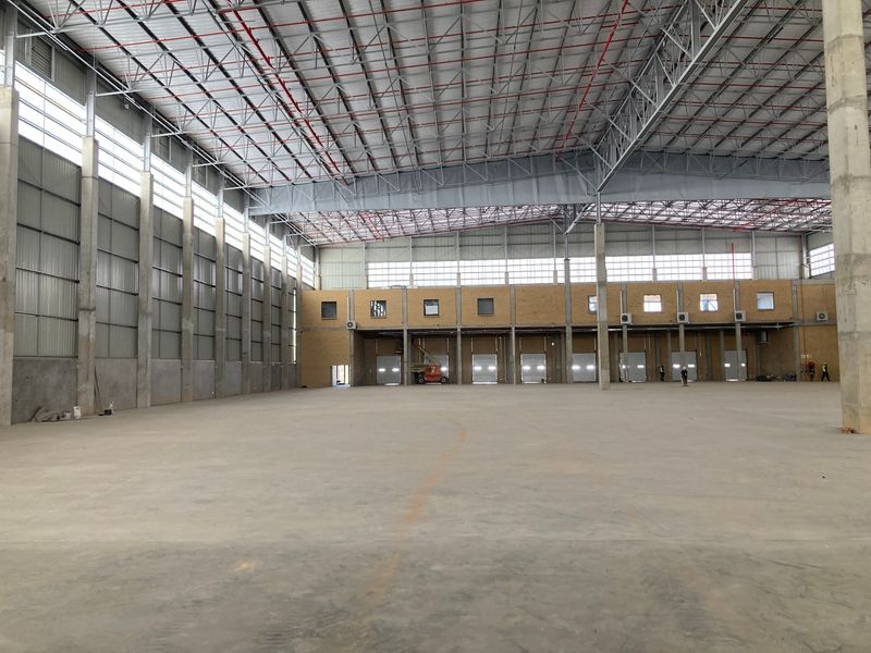 Spacious industrial warehouse featuring high ceilings, exposed steel trusses, concrete flooring, and multiple roller shutter doors for efficient loading and access.