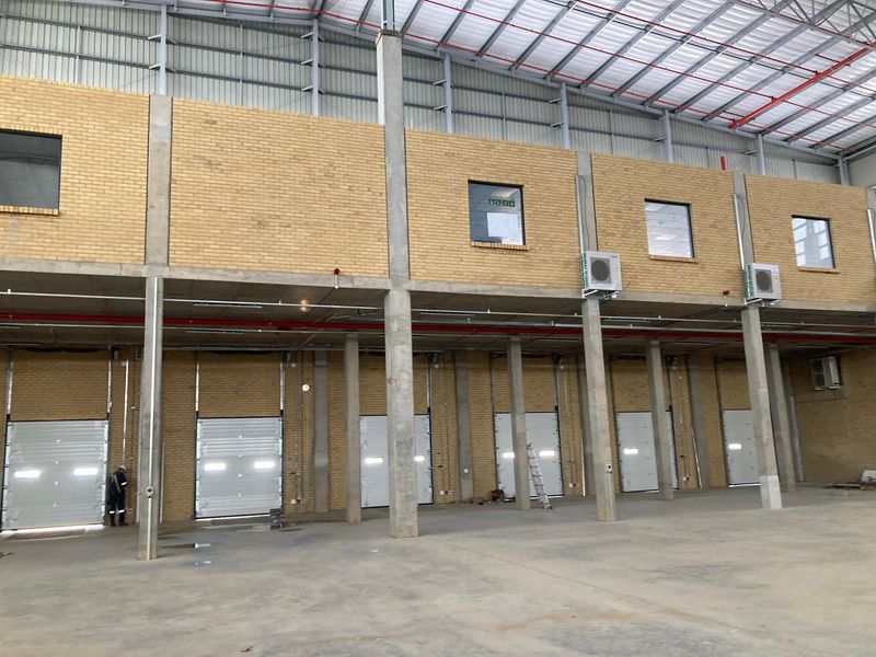 Spacious industrial warehouse interior featuring high ceilings, multiple roller shutter doors, exposed steel structure, and integrated fire suppression systems.