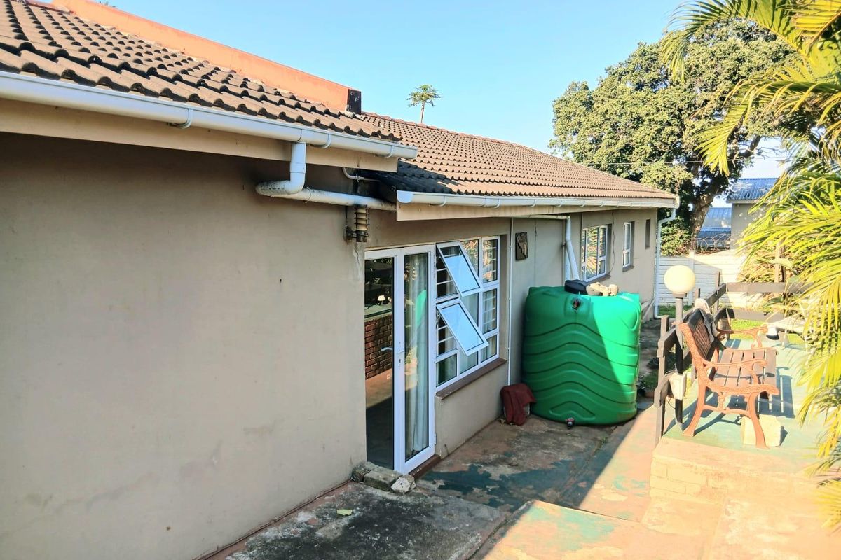 Rear exterior view of the house featuring a tiled roof, concrete patio area, and a large water storage tank.