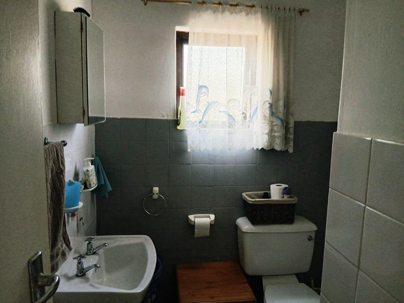 A functional bathroom featuring a pedestal basin, toilet, and tiled splashback, offering a dated aesthetic that could benefit from modern updates.
