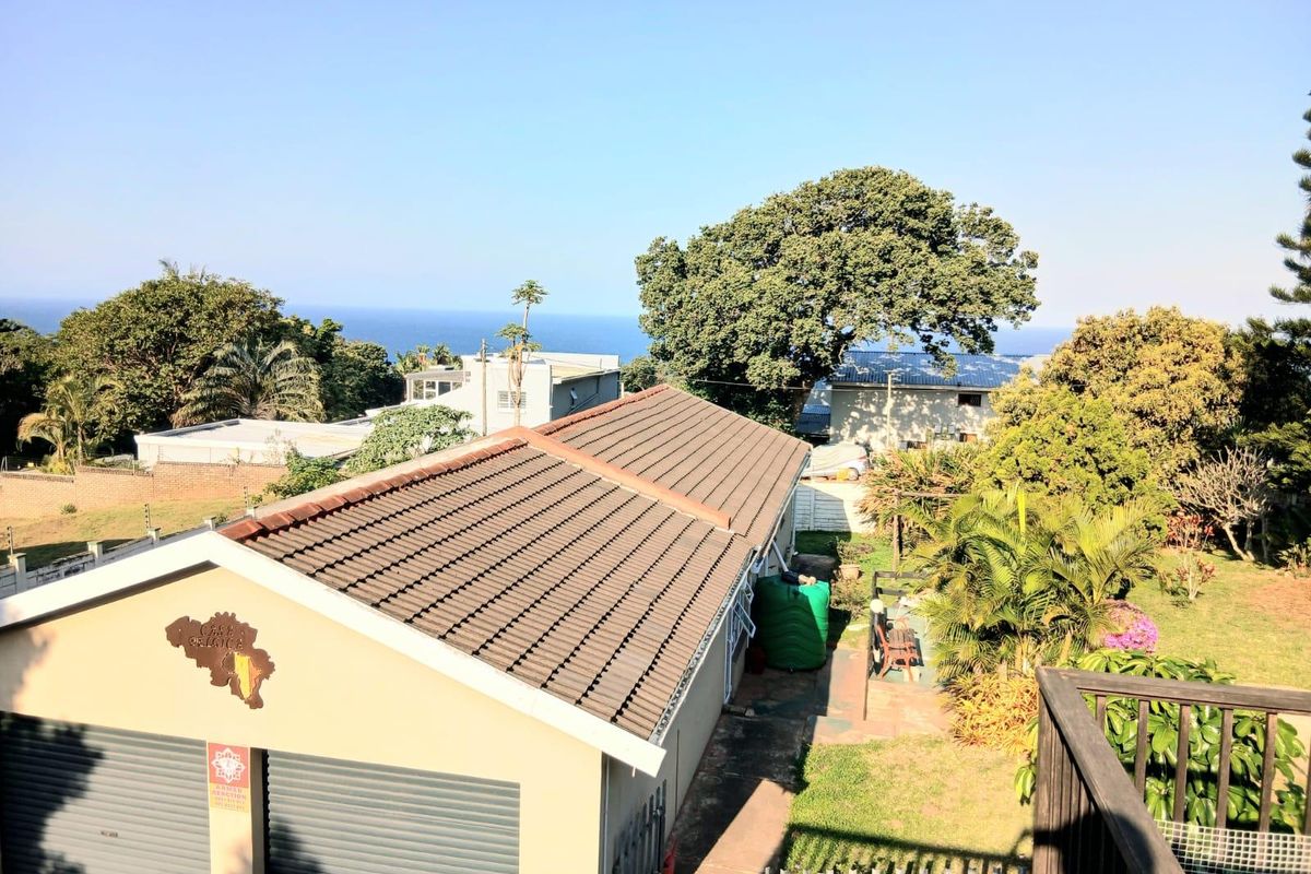 Aerial view of the property featuring a tiled roof garage, water storage tank, and a well-maintained garden with distant ocean views.