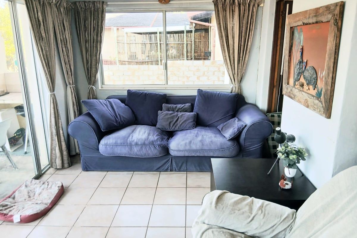 A sunlit living room featuring tiled flooring, a large window, and a sliding glass door providing access to the outdoor area.