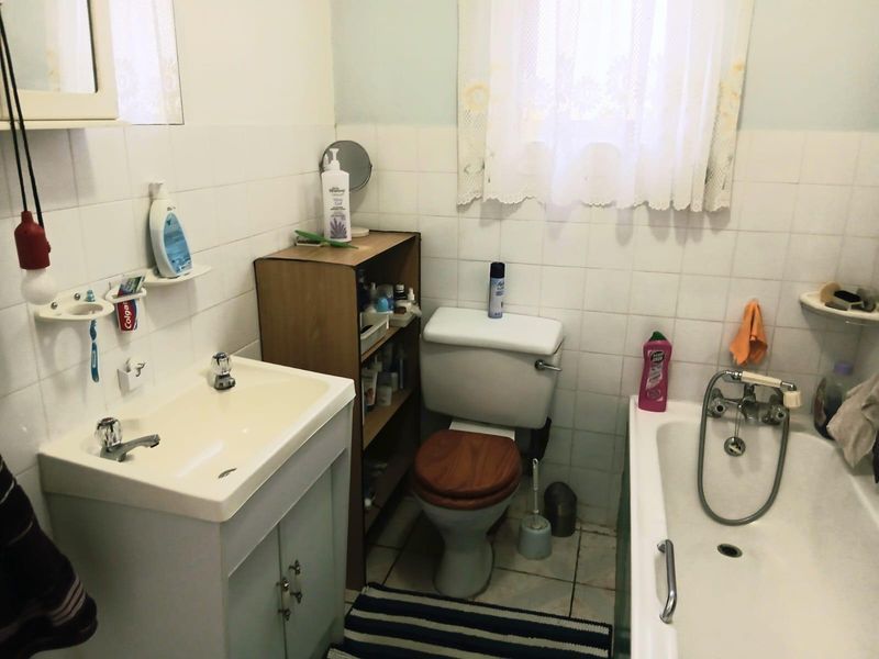 A functional bathroom featuring a vanity basin, toilet, and bathtub with wall-to-wall tiling, presenting an opportunity for modern cosmetic updates.